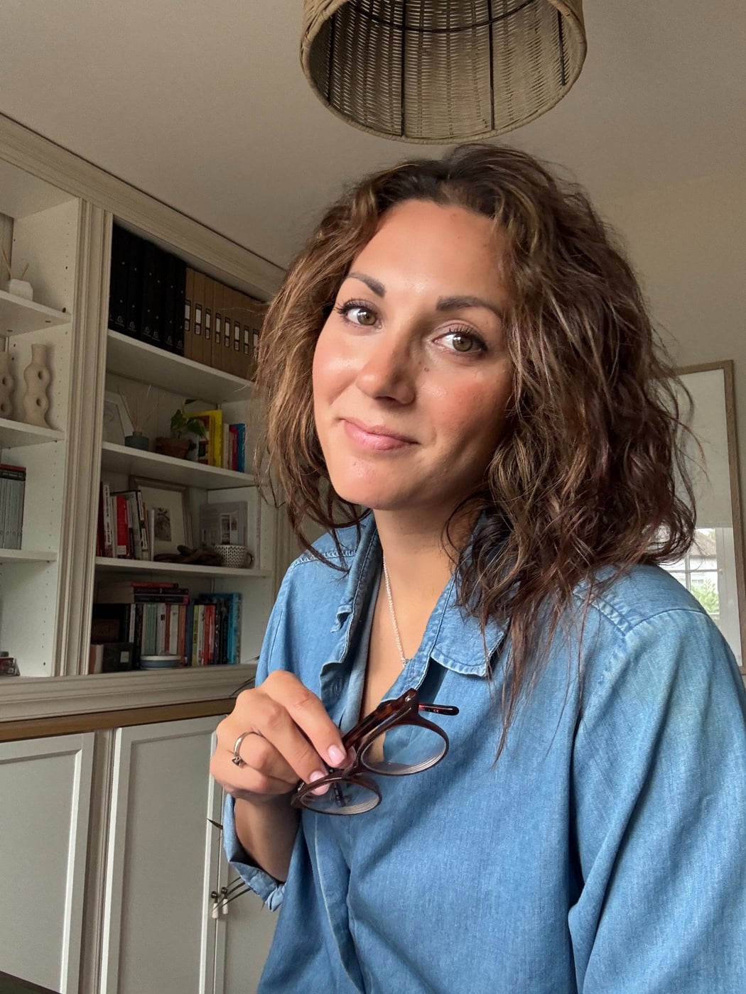 Jenna St John in her home office, holding her glasses